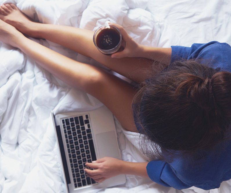 Woman sitting in bed with a cup of coffee and her laptop.